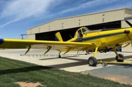 Yellow and blue agricultural aircraft parked in front of a hangar.