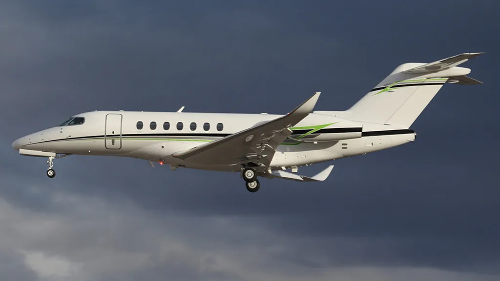 A white business jet with green and black stripes flying against a dark, cloudy sky with its landing gear extended.