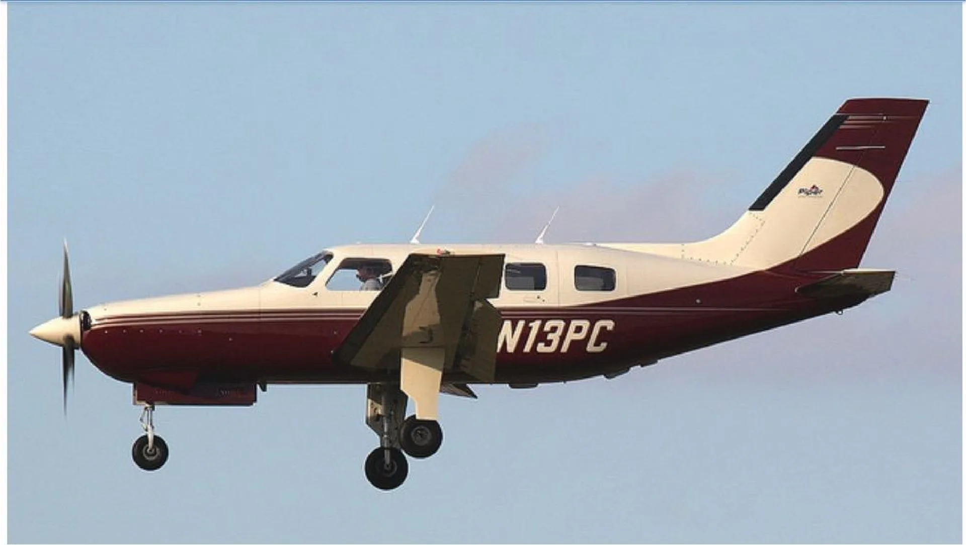 A Piper Malibu Mirage (N13PC) in maroon and cream paint scheme, flying with landing gear extended.