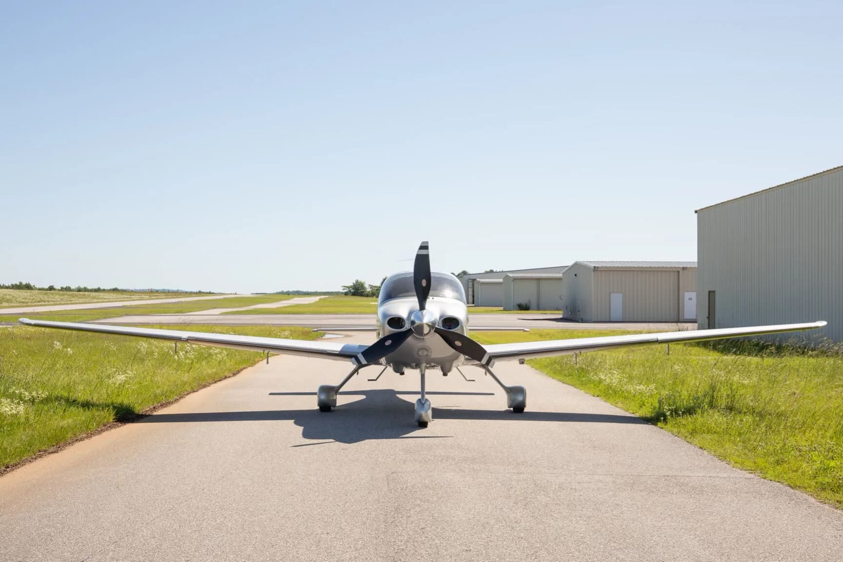 A silver Cirrus SR22T aircraft with registration N535J is viewed head-on, parked on an asphalt strip with hangars in the distance.