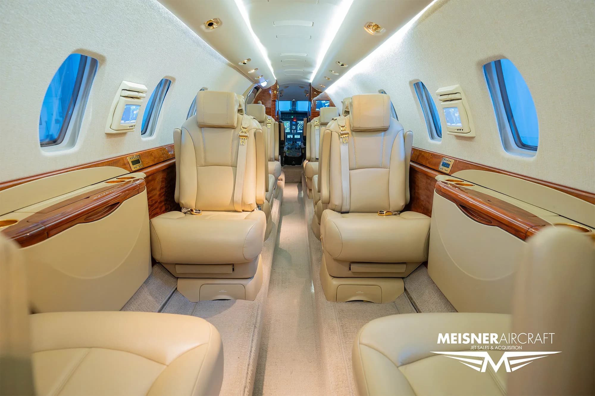The luxurious interior cabin of a business jet with beige leather seats and polished wood accents, looking forward to the cockpit.
