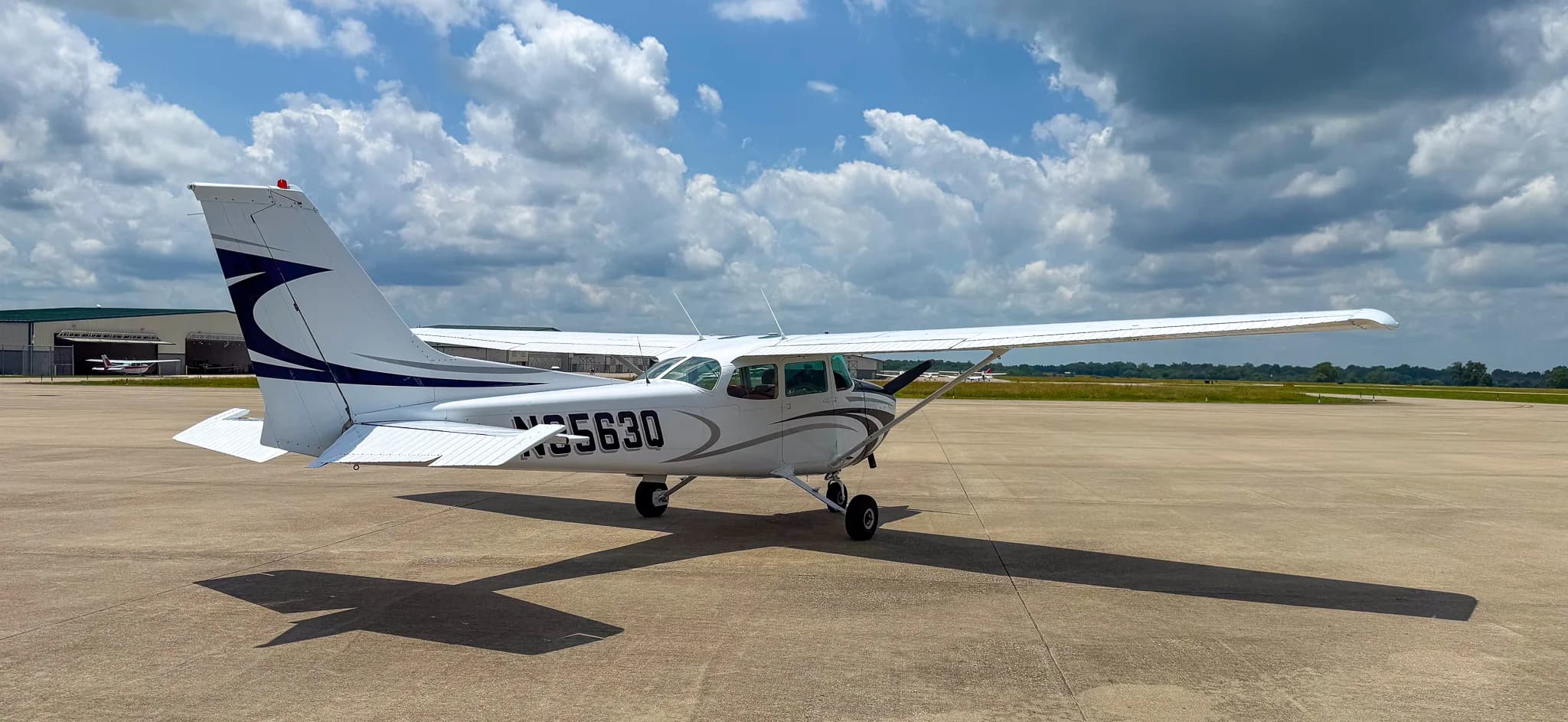 Right-rear view of a white and blue Cessna 172 with registration N3563Q on an airfield near a hangar.