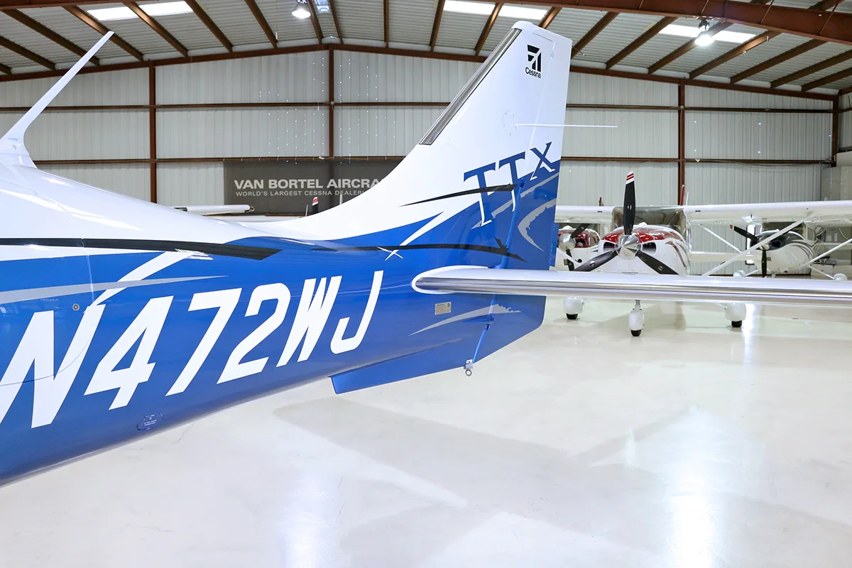 The blue and white tail section of a Cessna TTx aircraft, registration N472WJ, is shown in a hangar.