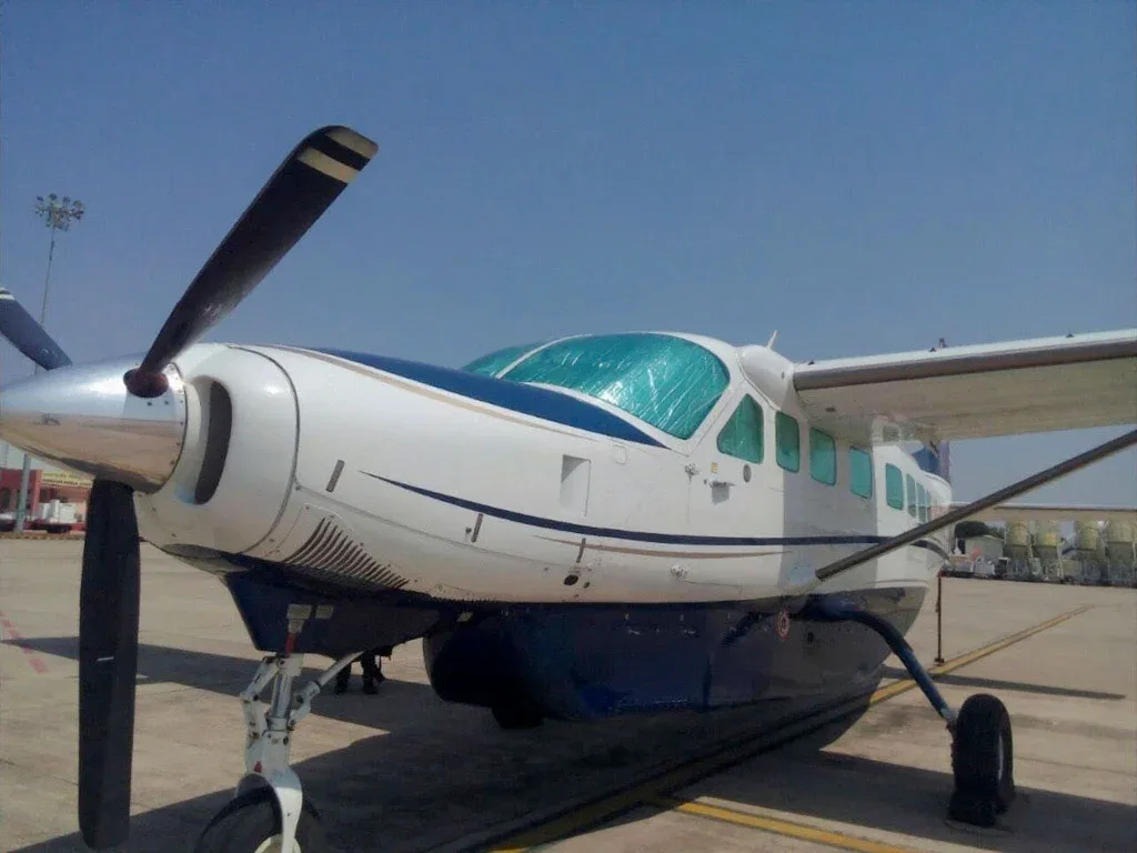 A close-up, low-angle view of the front of a white and blue single-engine turboprop aircraft with a large propeller, parked on an airfield.