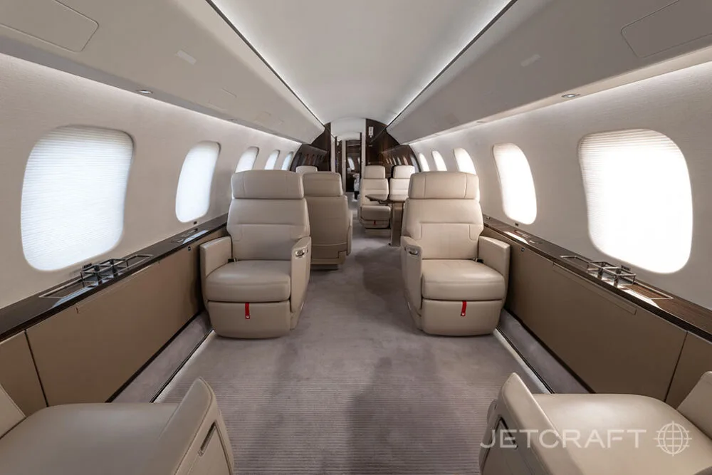 A luxurious aircraft cabin with light beige leather seats arranged in a club configuration, and large windows with shades.