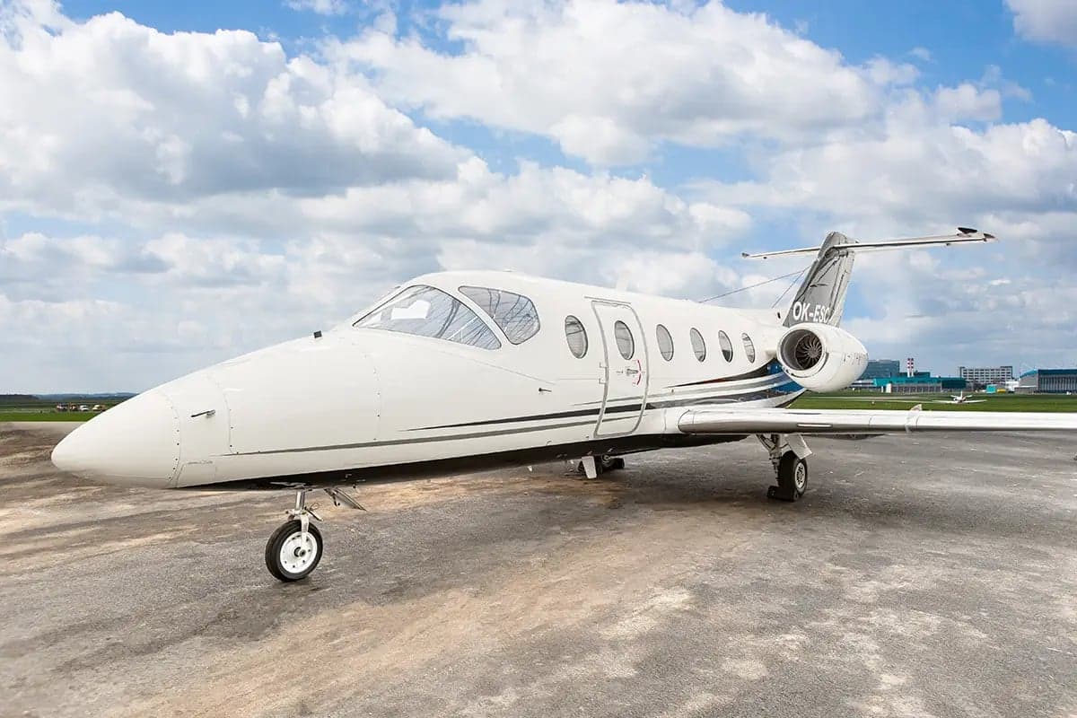 The Nextant 400XT aircraft with registration OK-ESC is parked on the tarmac with a cloudy sky in the background.