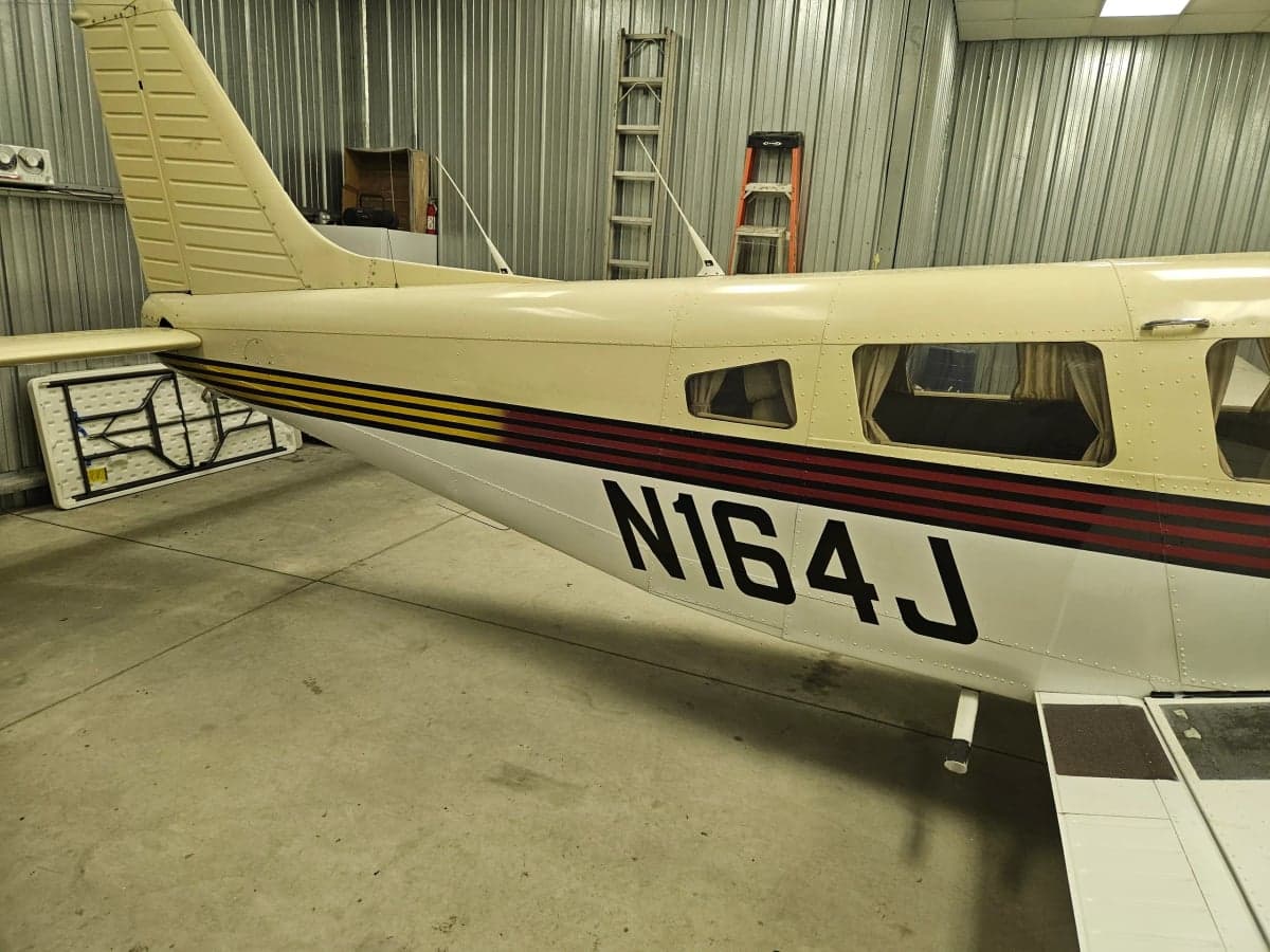 N164J, a light tan and white aircraft with red stripes, parked in a hangar.