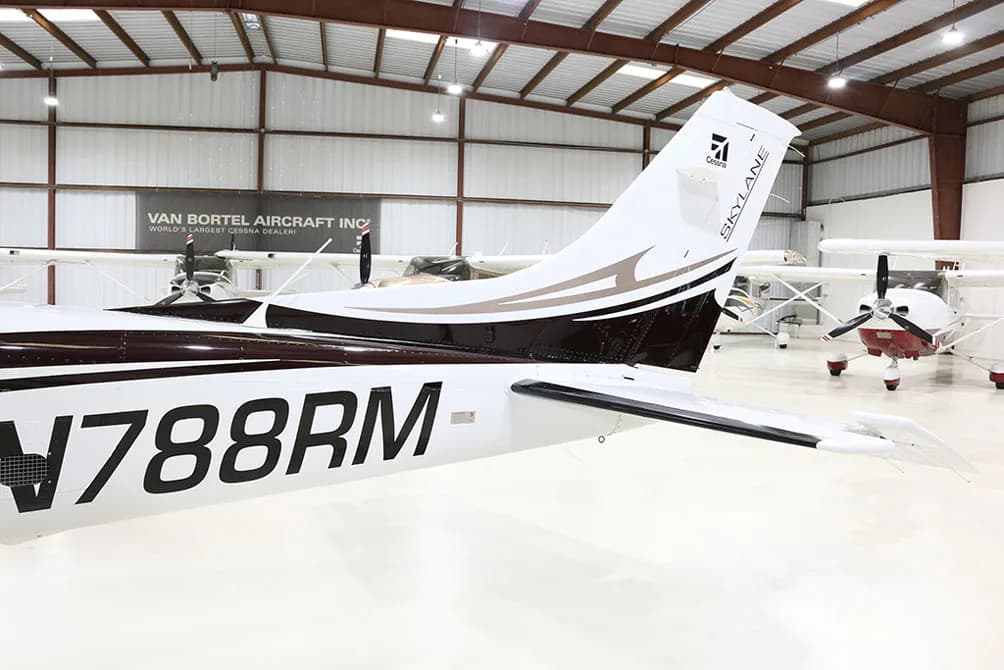 The tail section of a white and brown Cessna Skylane N788RM is shown in a hangar.