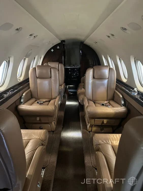 The interior cabin of a private jet with tan leather seats arranged in a club configuration.