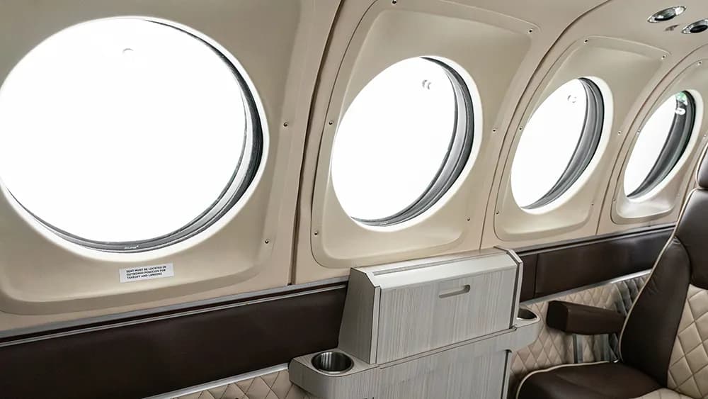 A row of circular aircraft windows and a fold-out table with cup holders in the cabin.