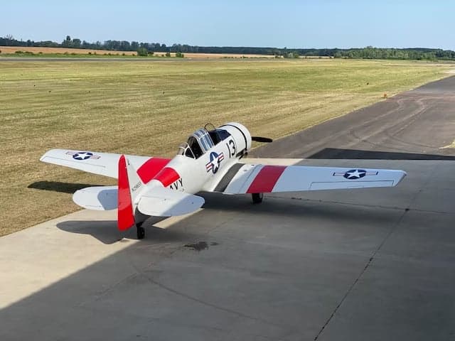 A white and red North American Aviation T-6 Texan aircraft is parked on a runway, viewed from the rear.
