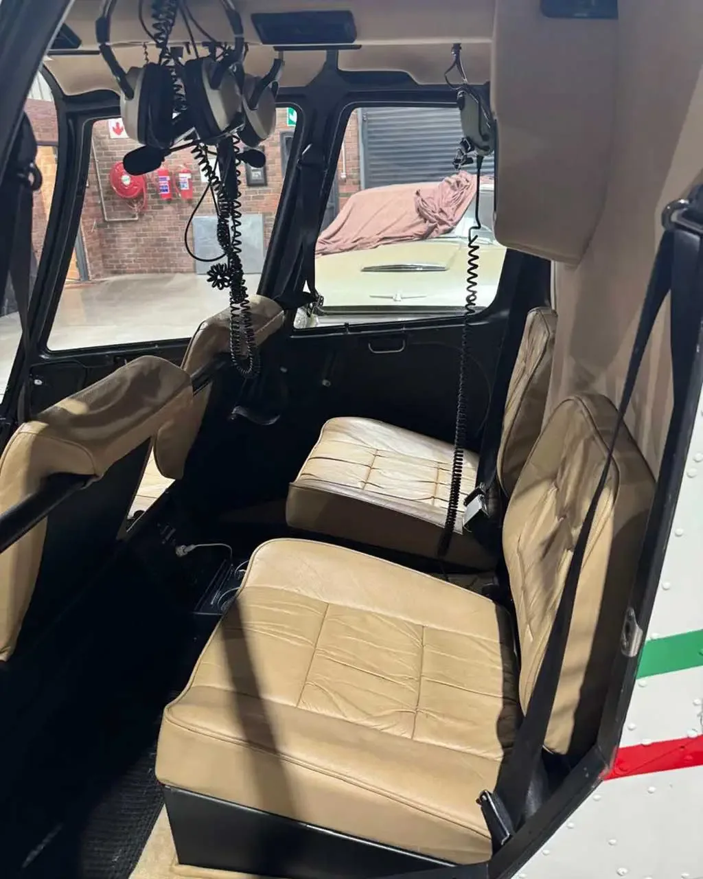 The tan leather interior seats of a helicopter are visible, with headsets hanging from the ceiling.