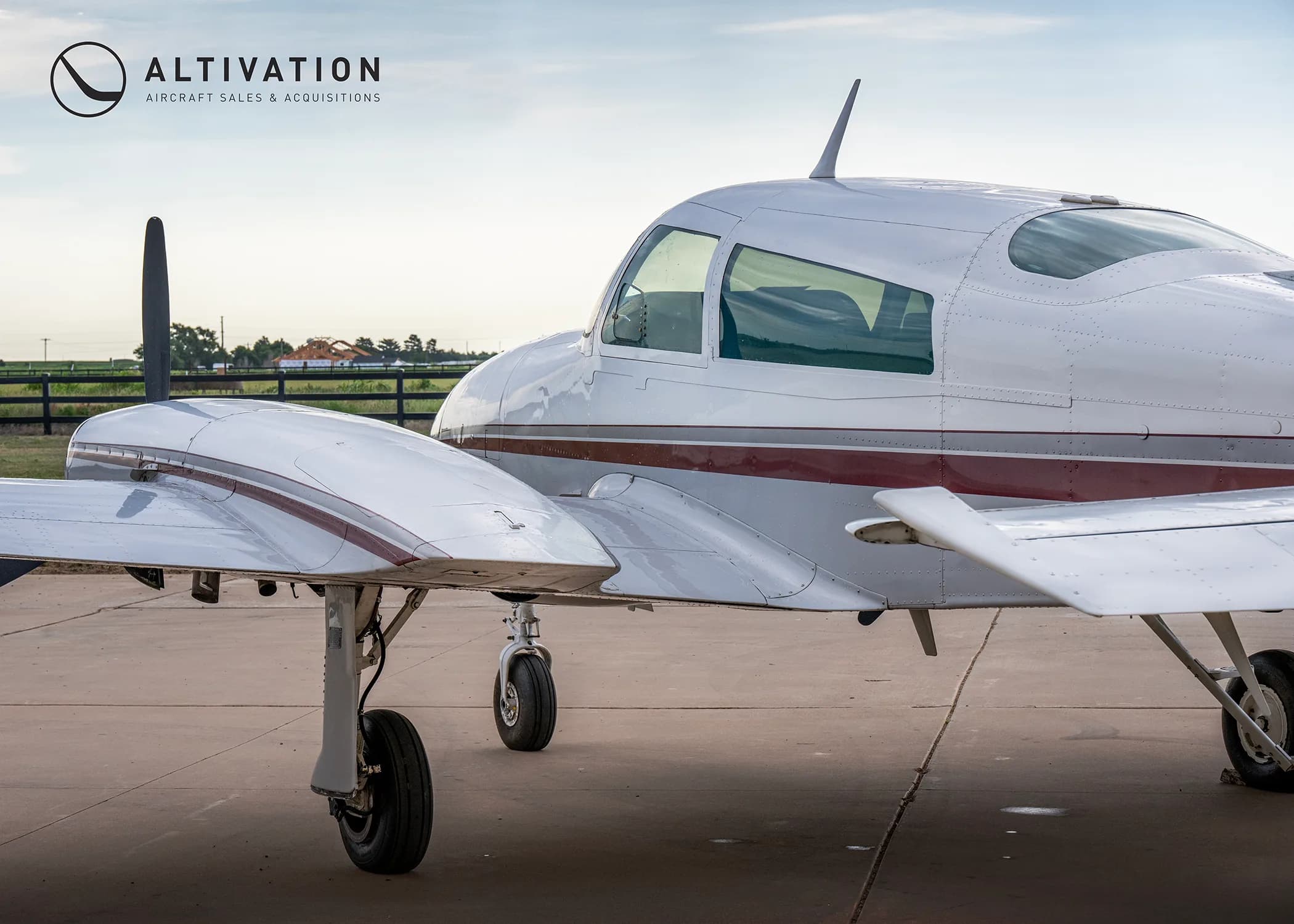 A close-up side view of the fuselage and right engine of a white twin-engine propeller aircraft with maroon stripes.