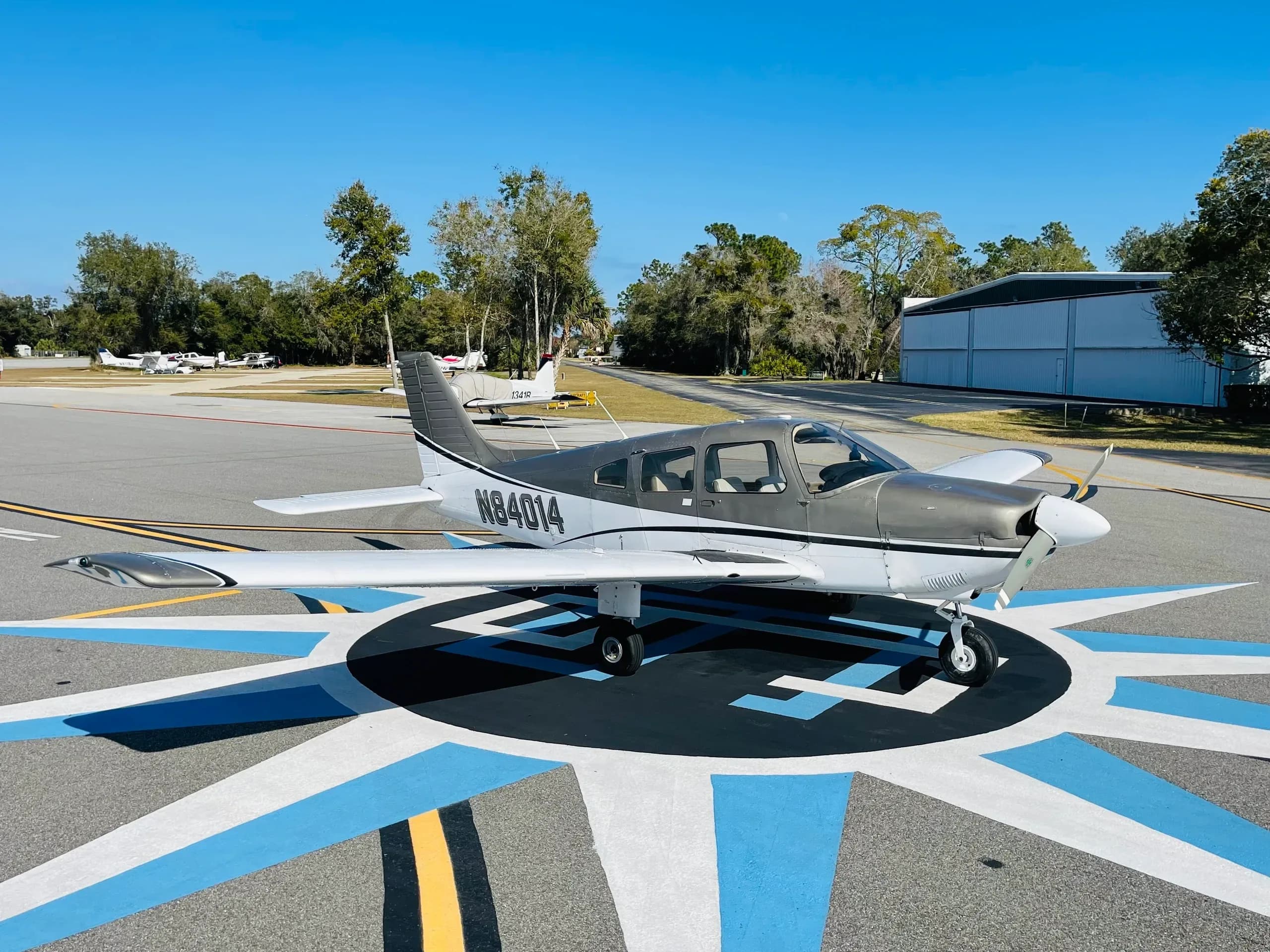 A gray and white single-engine aircraft, registration N84014, parked on a blue and white marked tarmac at an airfield.