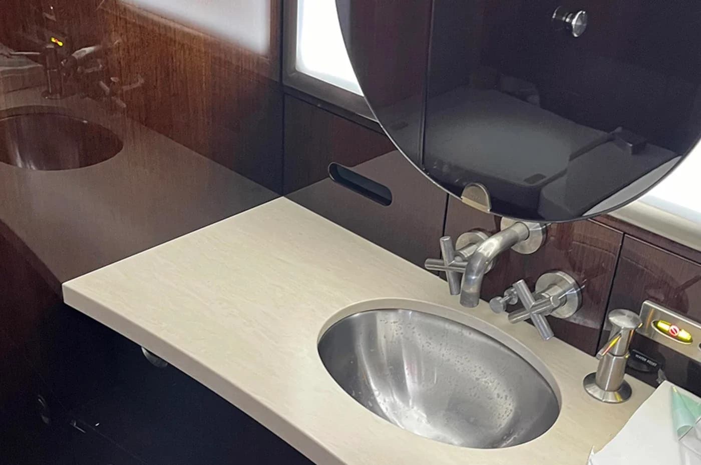 A close-up of the aircraft lavatory, showing a modern sink with chrome fixtures and a mirror, surrounded by dark wood paneling.