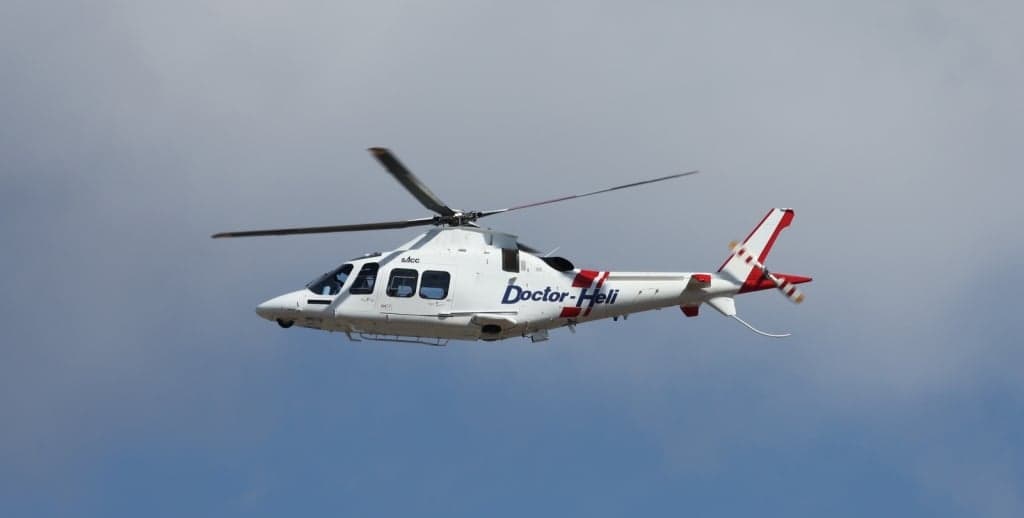 A white and red AgustaWestland AW109 helicopter with 'Doctor-Heli' livery in flight.