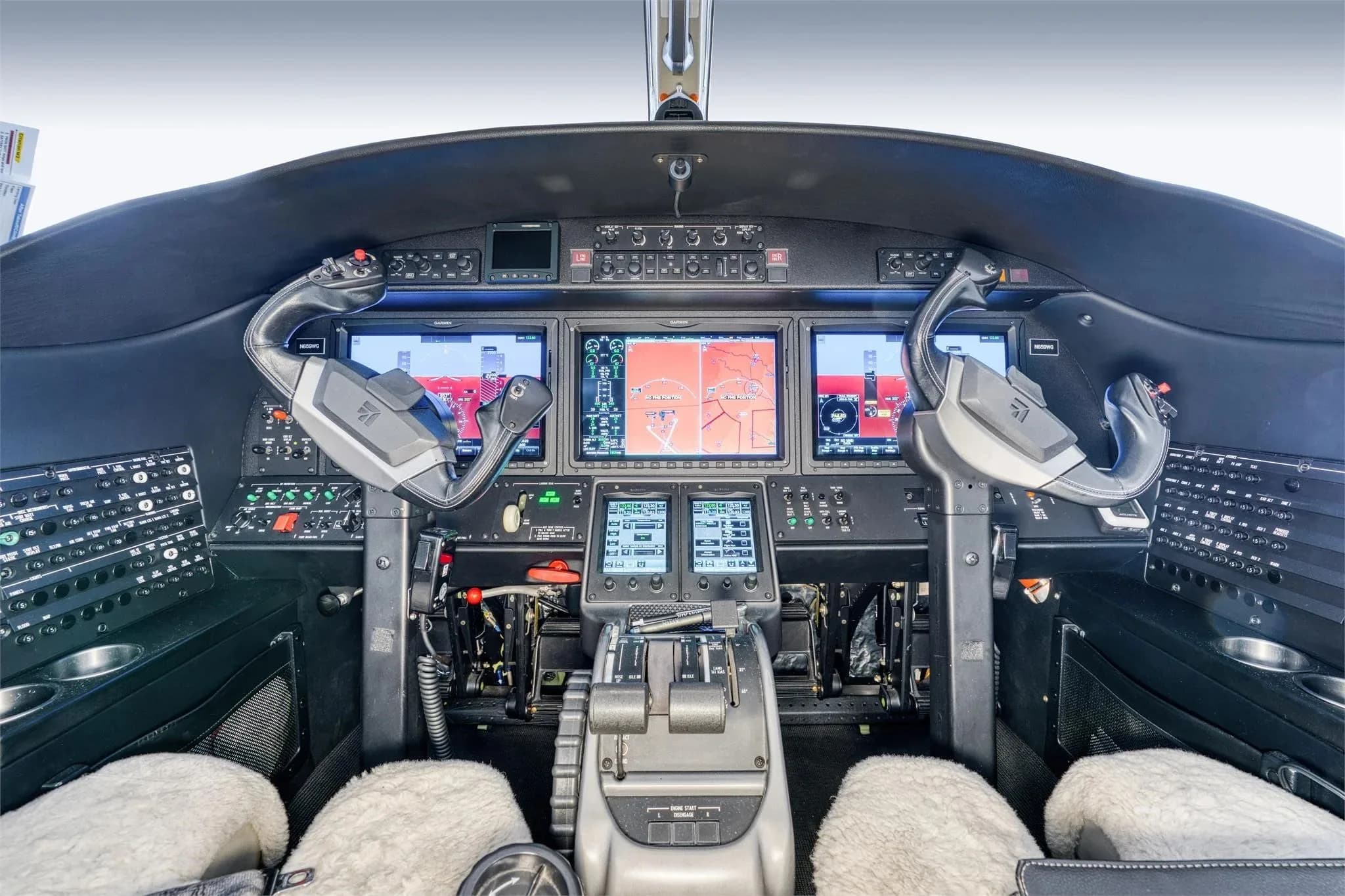 A modern aircraft cockpit with multiple large display screens and two yokes, seen from the pilot's seat.