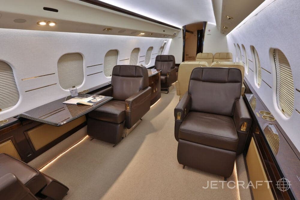 A wide-angle view of the business jet cabin, showing multiple brown leather seats and a table with a book.