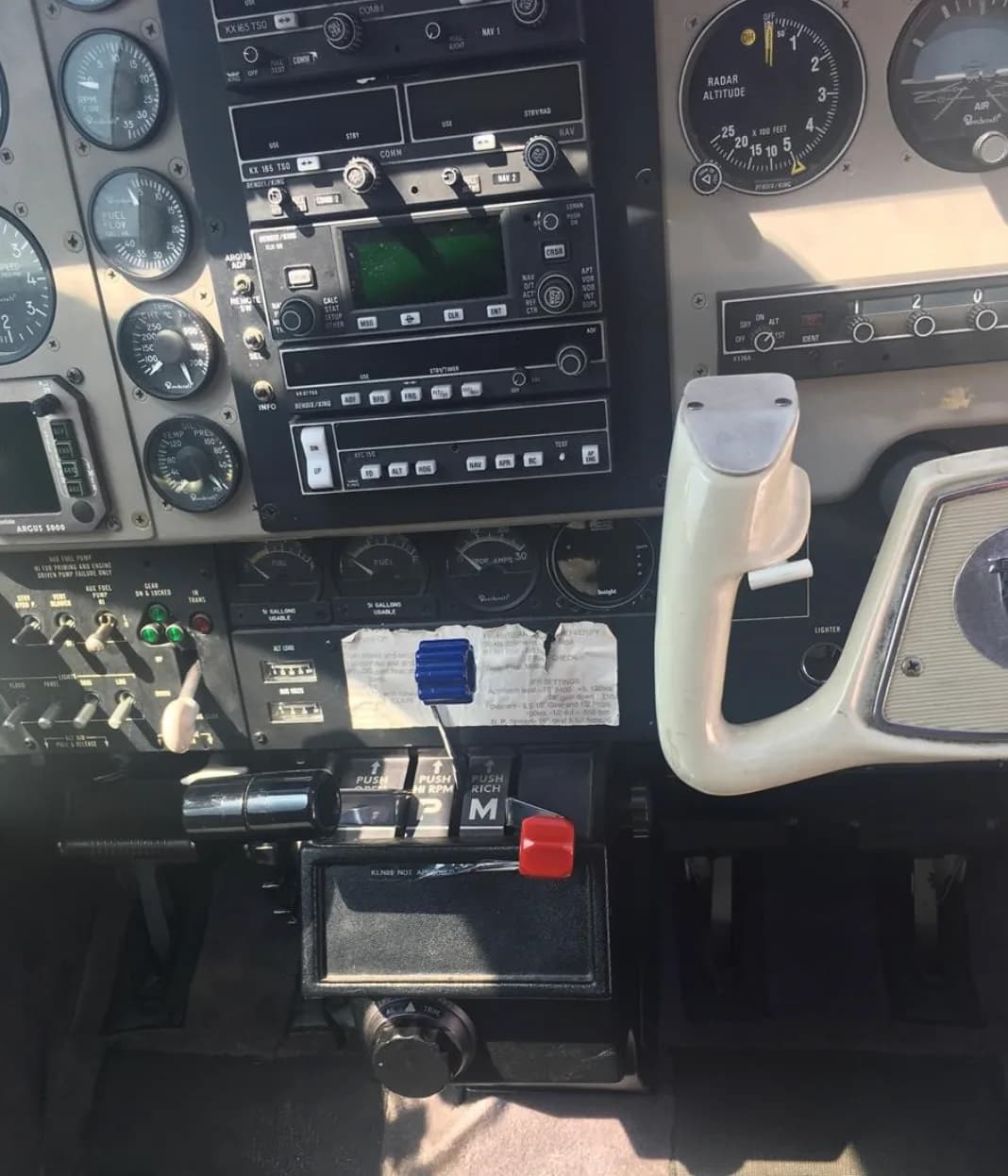 A close-up of the lower instrument panel, radio stack, and engine controls in a Beechcraft Bonanza cockpit.