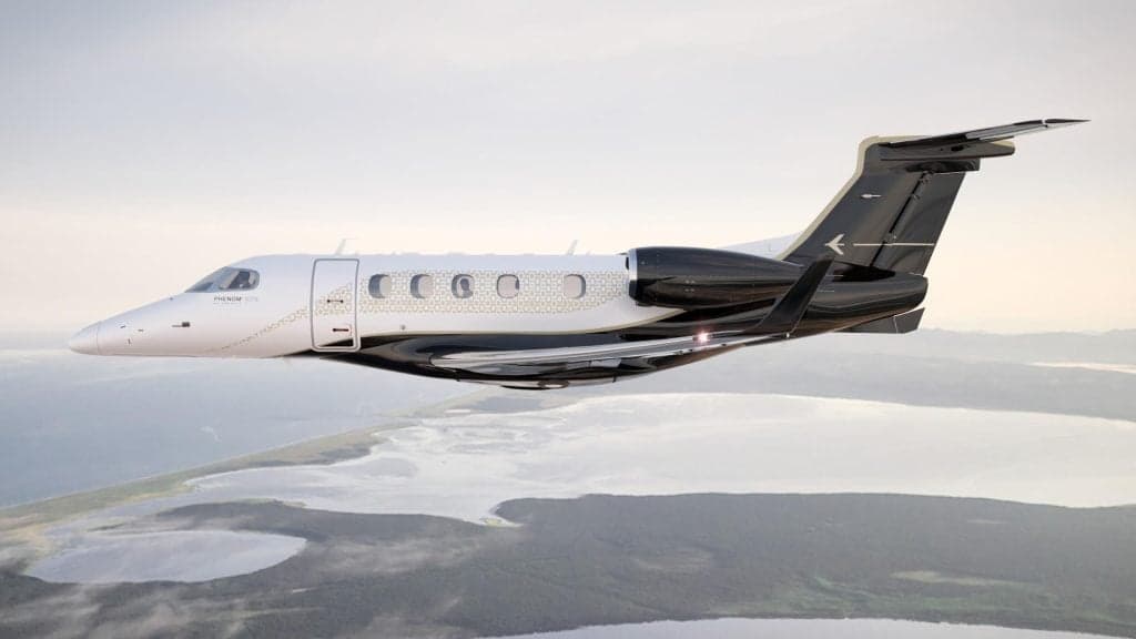 A Phenom 300E aircraft in flight over a coastal landscape.