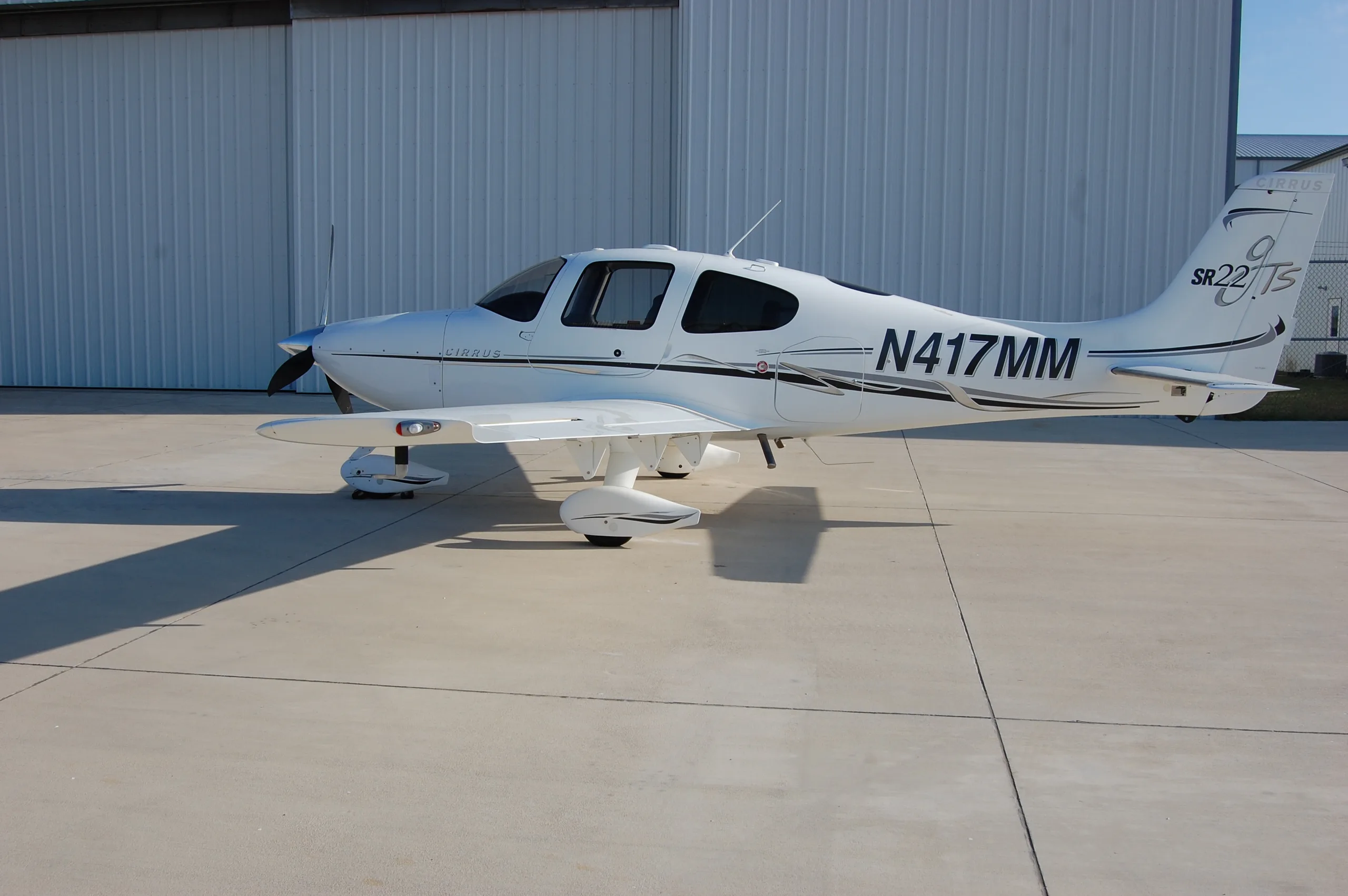 A side view of the white Cirrus SR22 aircraft, N417MM, parked on an airfield.