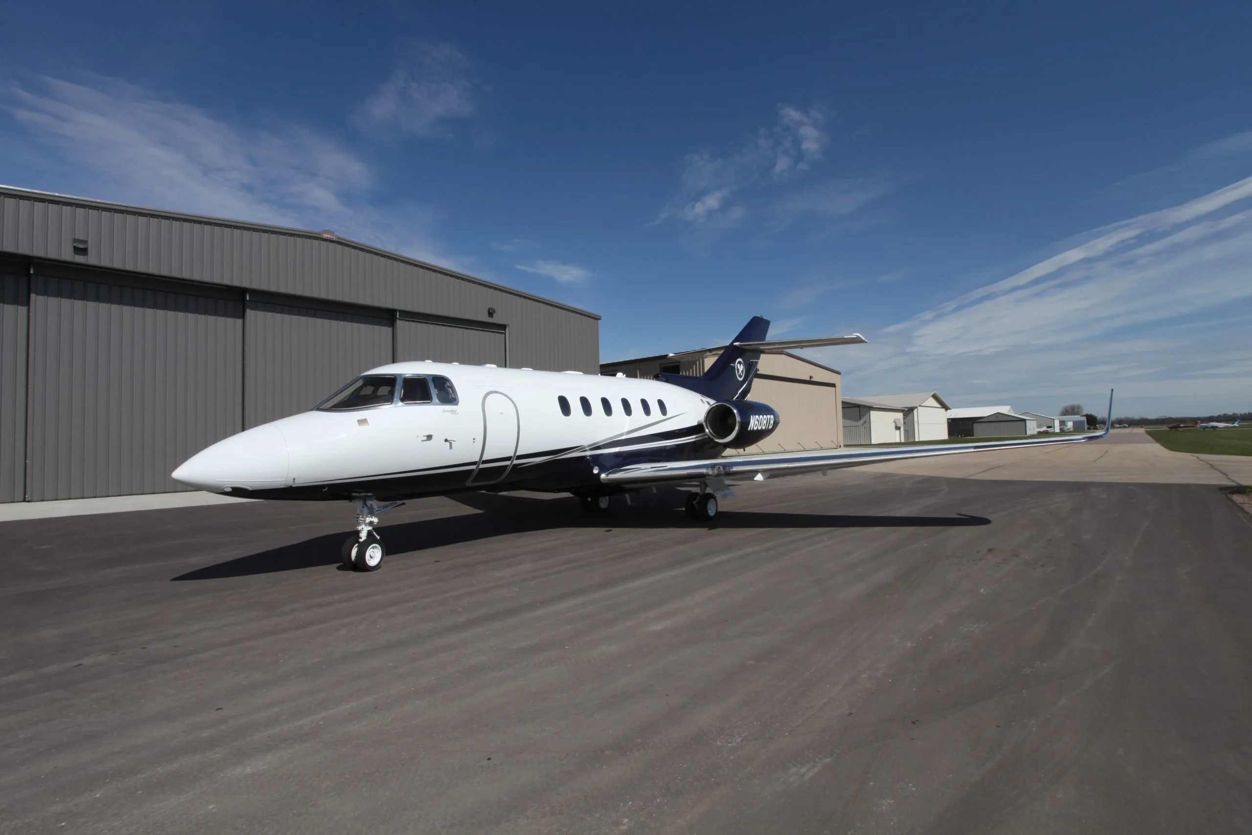 A Hawker 400XP aircraft is parked on the tarmac in front of a hangar on a sunny day.