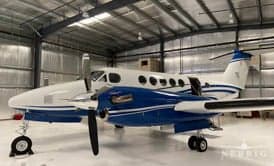A white and blue Beechcraft King Air turboprop aircraft parked inside a hangar.