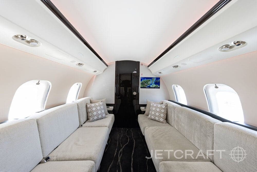 Aft view of the cabin of a Bombardier Global Express with light colored couches and patterned pillows.
