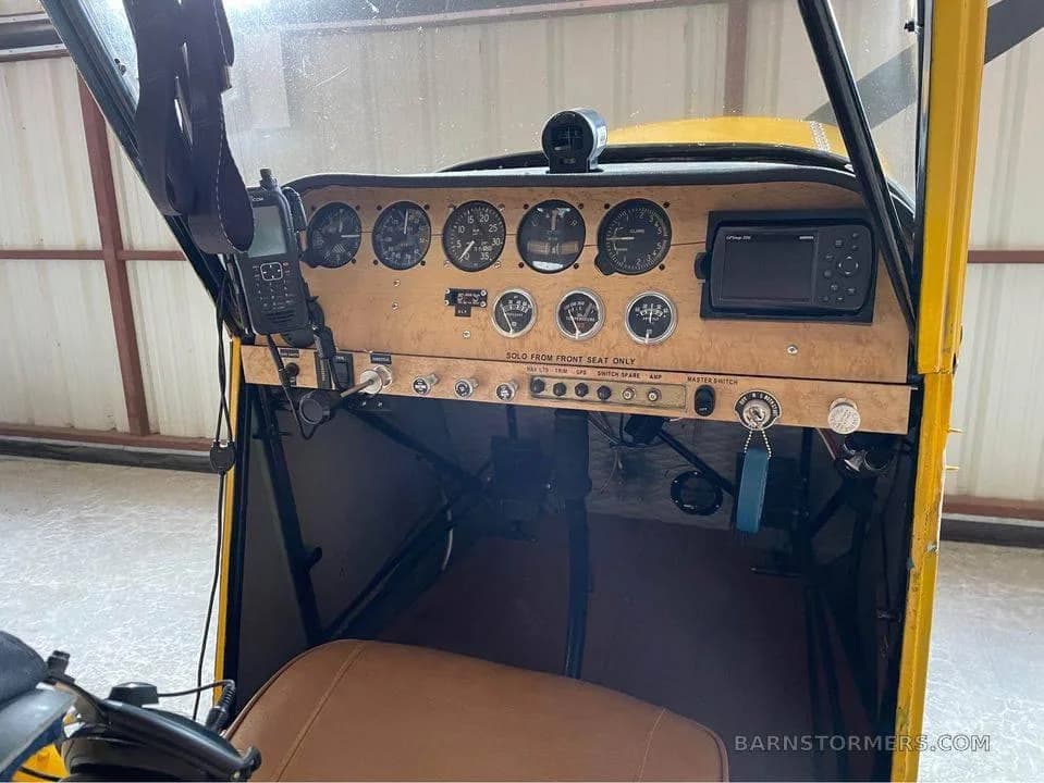 The cockpit of a yellow aircraft, featuring a wooden instrument panel with gauges and a GPS unit.
