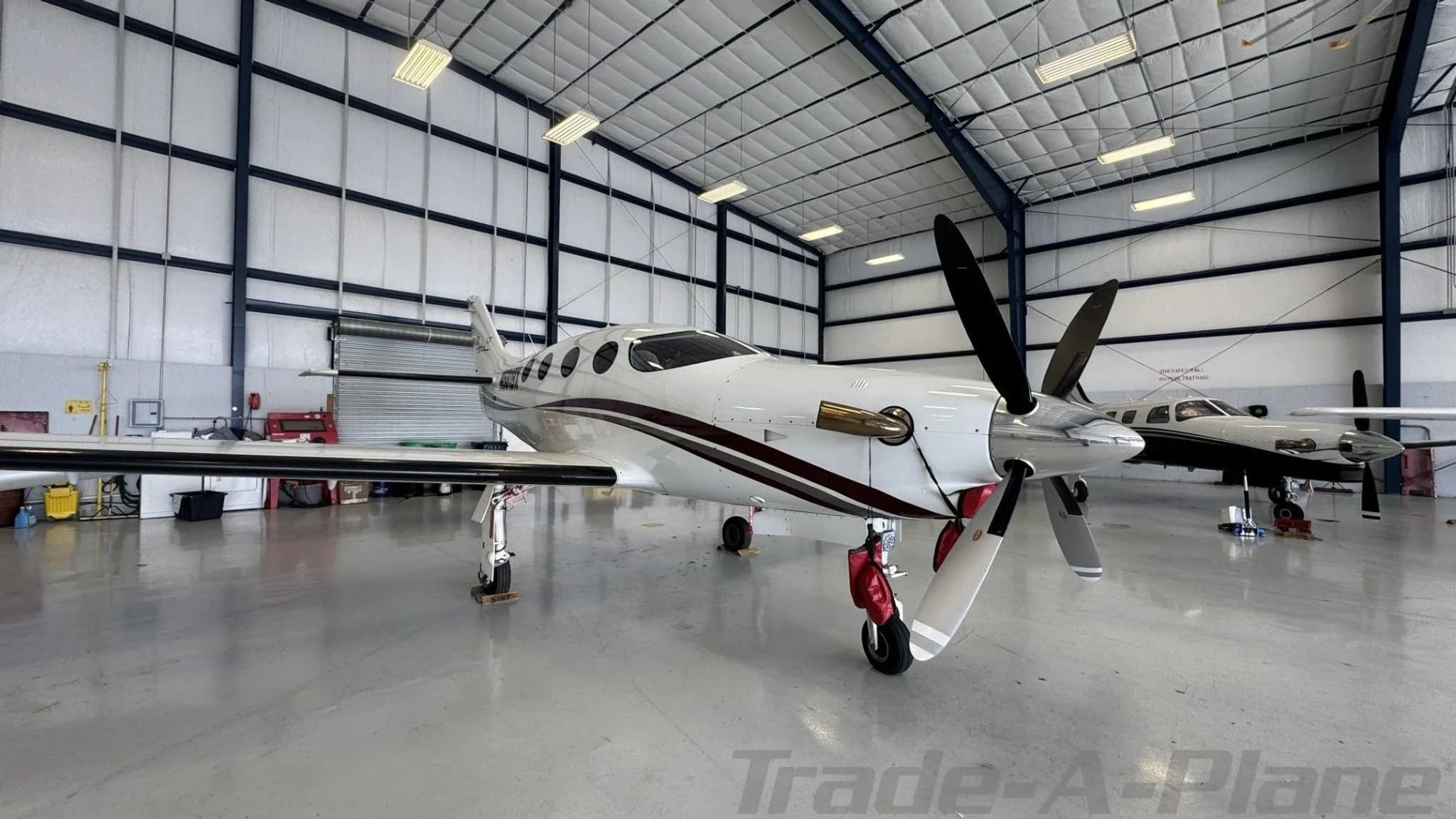 Three-quarter front view of a white Epic LT aircraft with a dark red stripe, parked in a hangar.