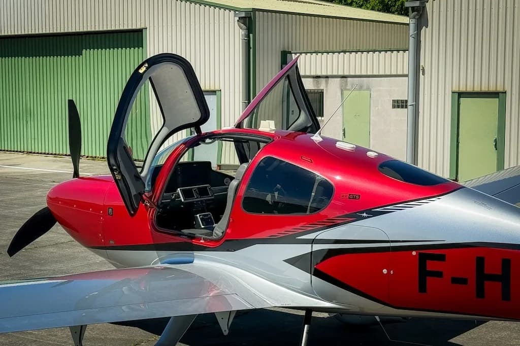 A red and silver Cirrus SR22 GTS with both gull-wing doors open, revealing the cockpit and interior.