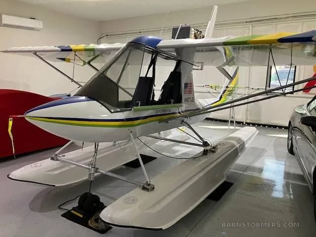 A white and blue experimental floatplane with yellow and green wing accents, parked in a hangar.