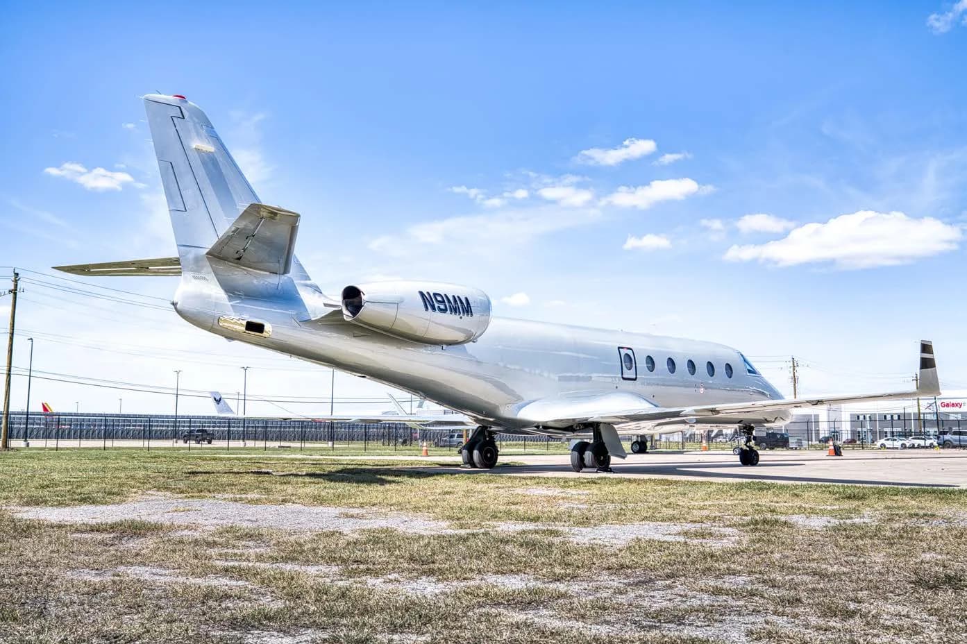 A silver business jet with registration N9MM parked on an airfield, viewed from the rear-right.