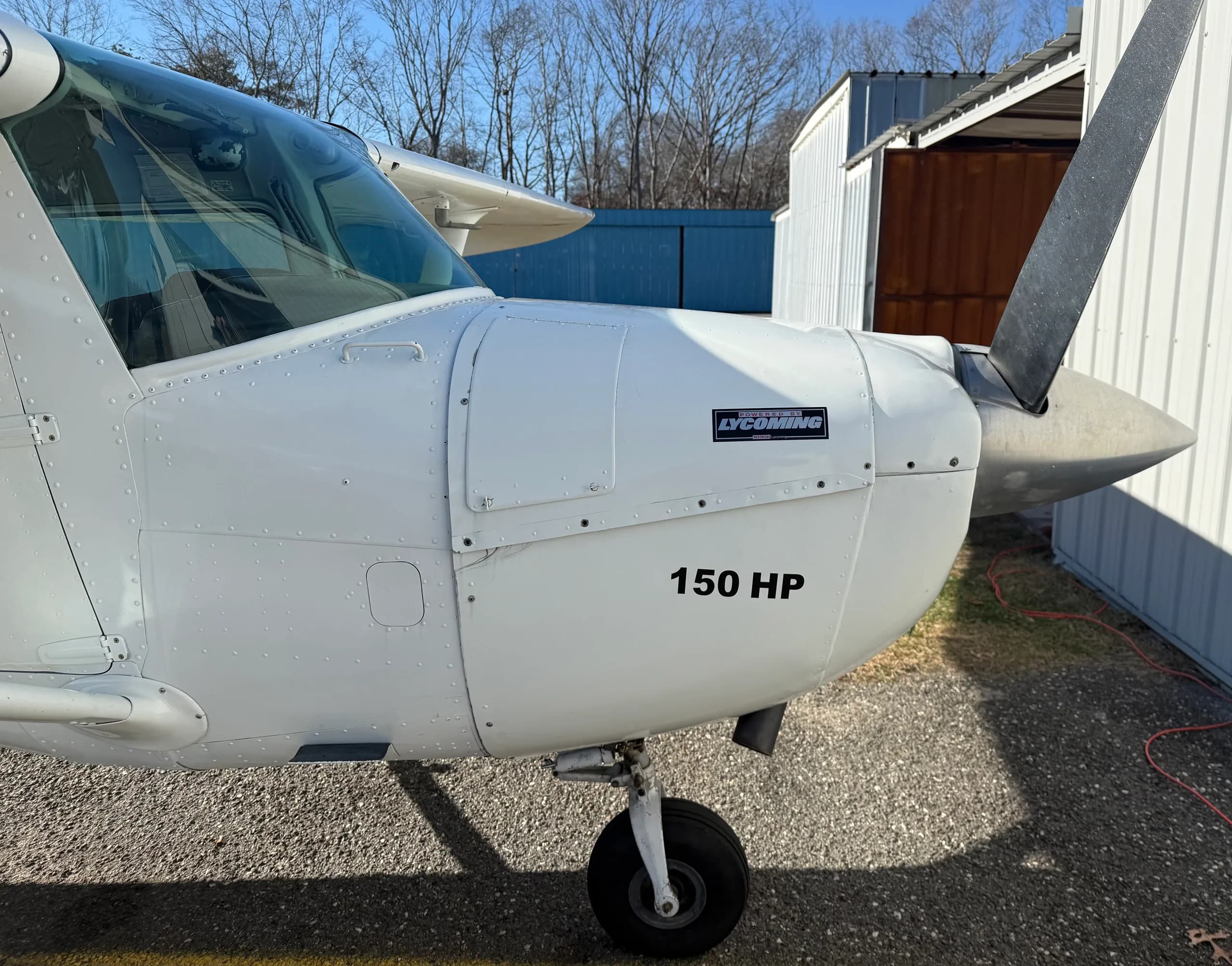 A front-side view of the white Cessna 150 aircraft, showing the propeller, engine cowling with "150 HP" text, and nose wheel.