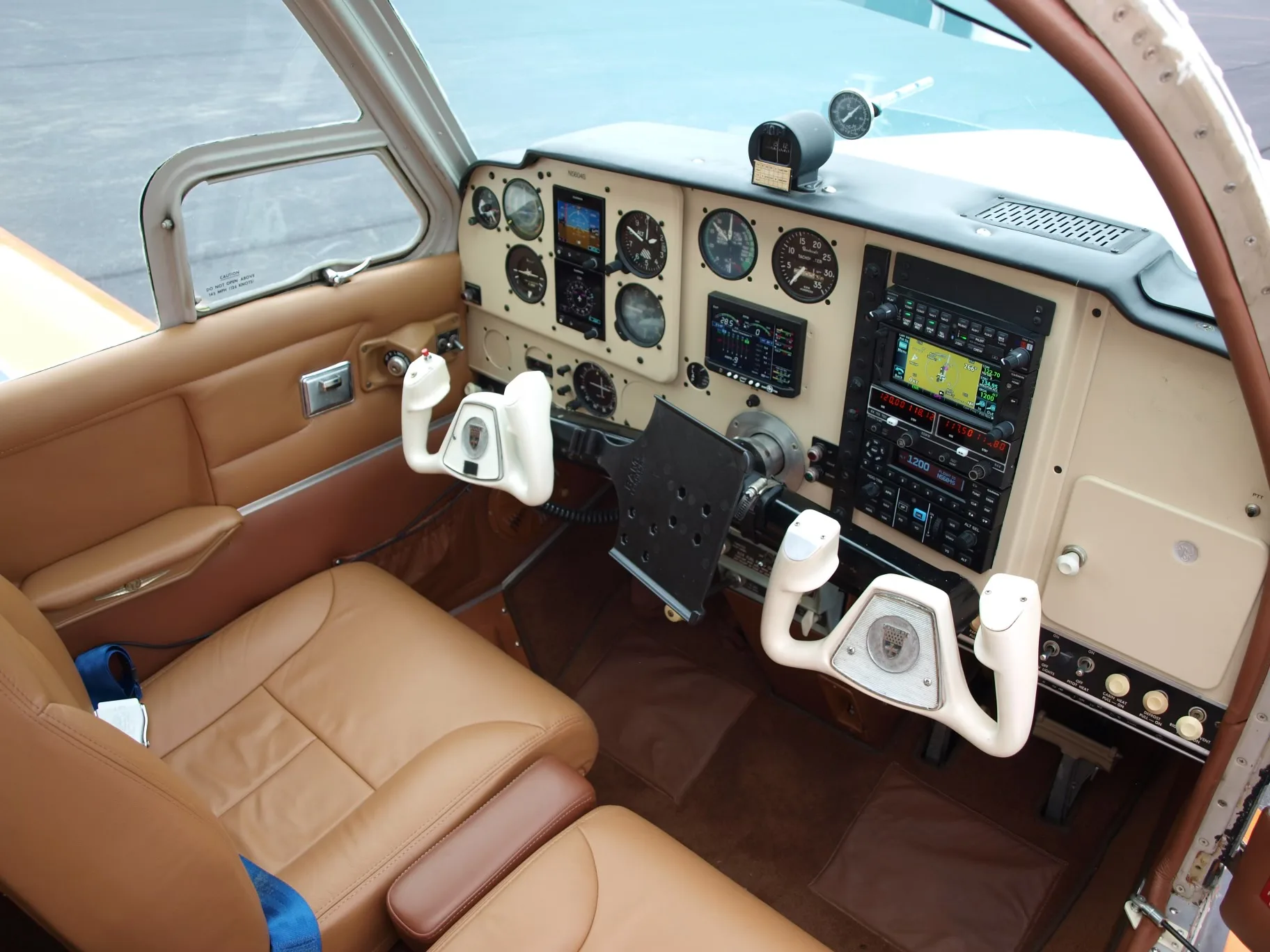 The cockpit of a Beechcraft V35 Bonanza aircraft, showing the instrument panel, control yokes, and seats.