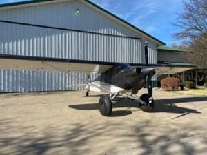 A Carbon Cub aircraft is parked on a concrete pad in front of a building.