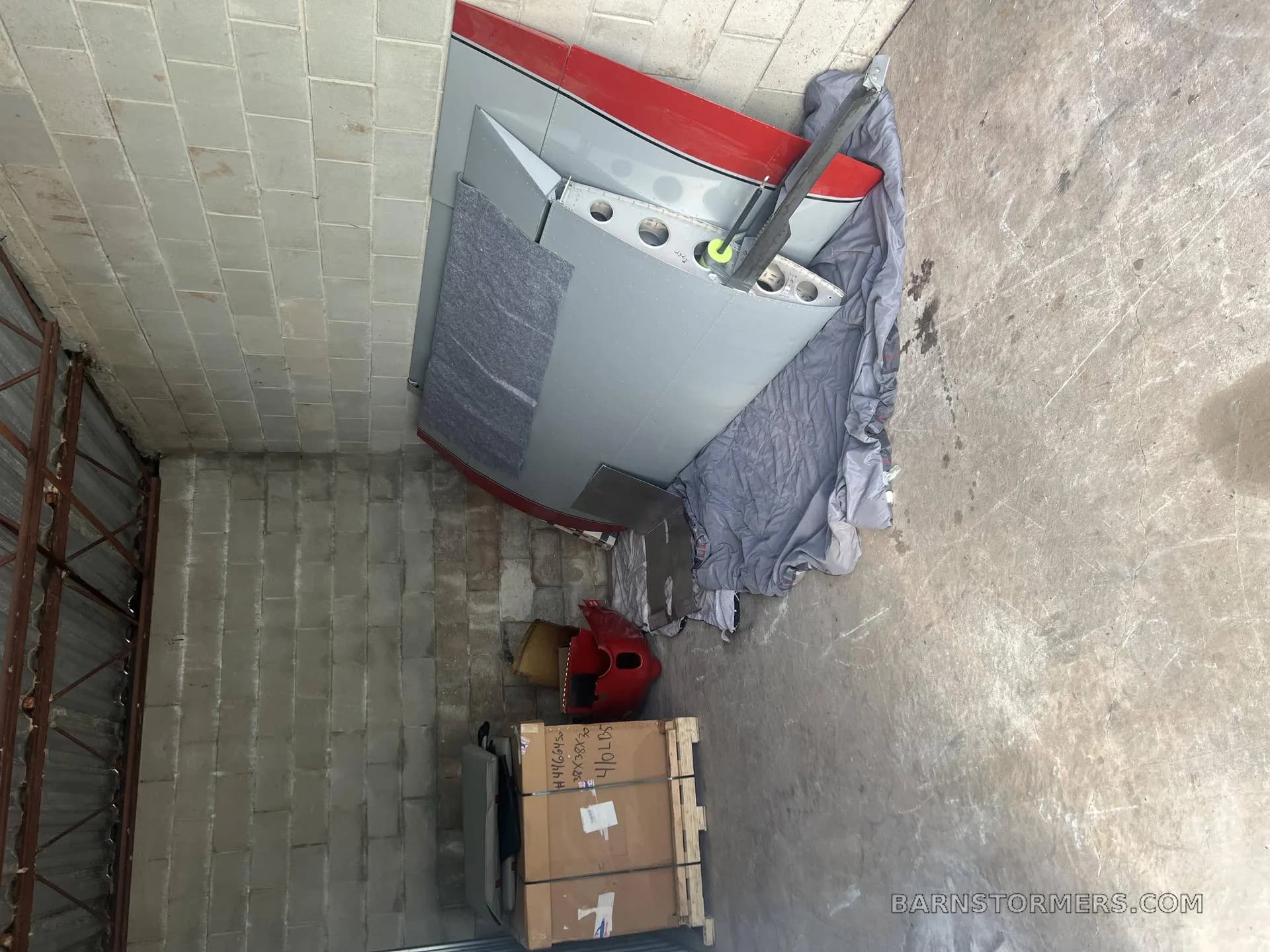 Disassembled aircraft wing and tail components with red accents, stored on a concrete floor.