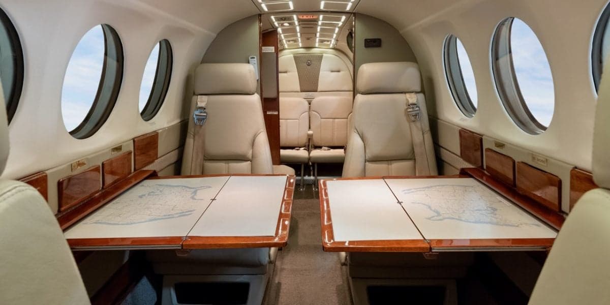 The luxurious interior cabin of a Beechcraft King Air, N508SK, with beige leather seats and two tables with maps.