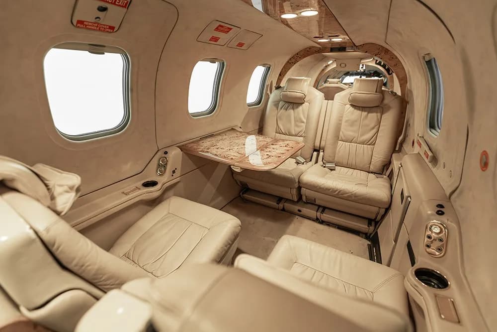 The luxurious beige leather interior cabin of the N220MA aircraft, with seating and a fold-out table.