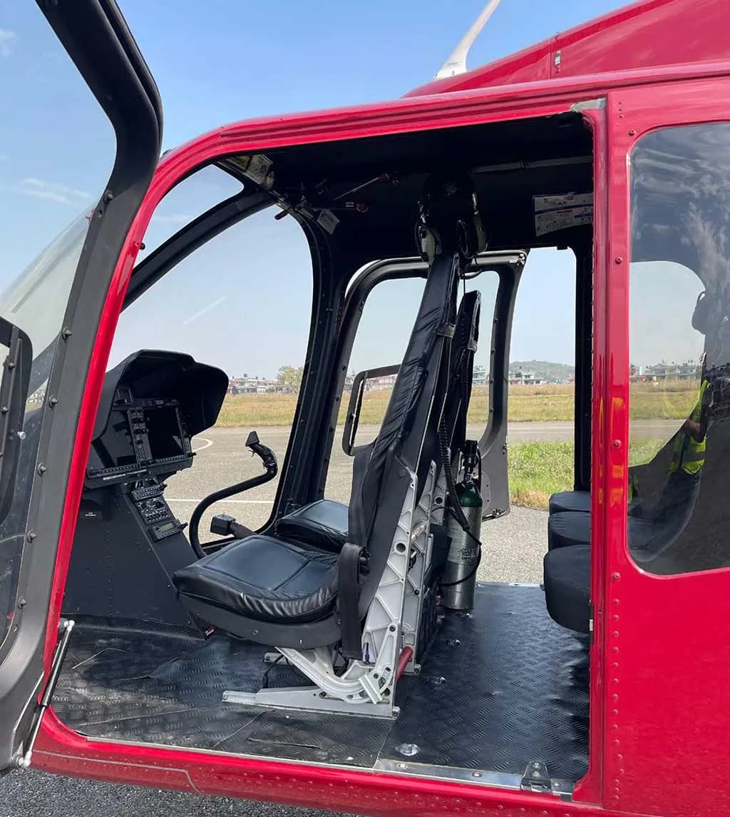 The open door of a red helicopter reveals the pilot's seat, part of the instrument panel, and the cabin interior.