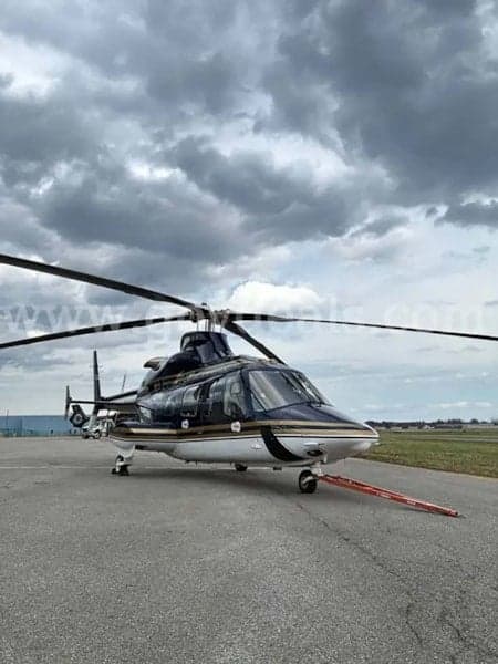 A black and white helicopter is parked on the tarmac under a cloudy sky.