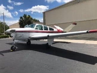 A Beechcraft Bonanza with a white and red paint scheme is parked on the tarmac.