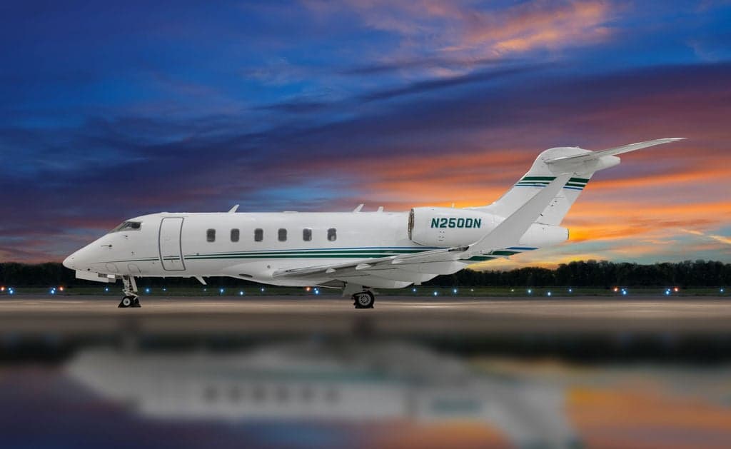 Side view of a white and green aircraft with registration N250DN on the runway at sunset.