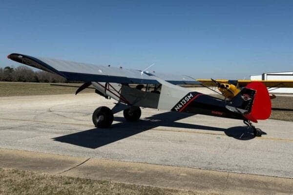 Side view of the gray and red N413SM aircraft parked on the tarmac on a sunny day.