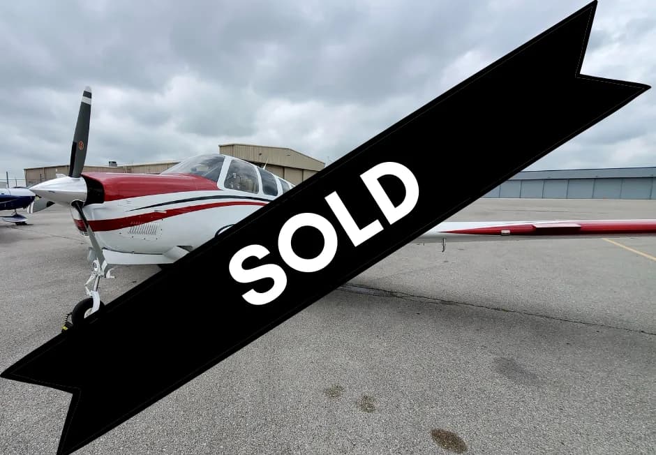 A white and red single-engine propeller aircraft is parked on an asphalt tarmac under a cloudy sky.