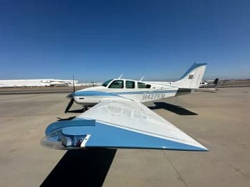 A Beechcraft Bonanza with blue and white paint scheme is parked outside a hangar.
