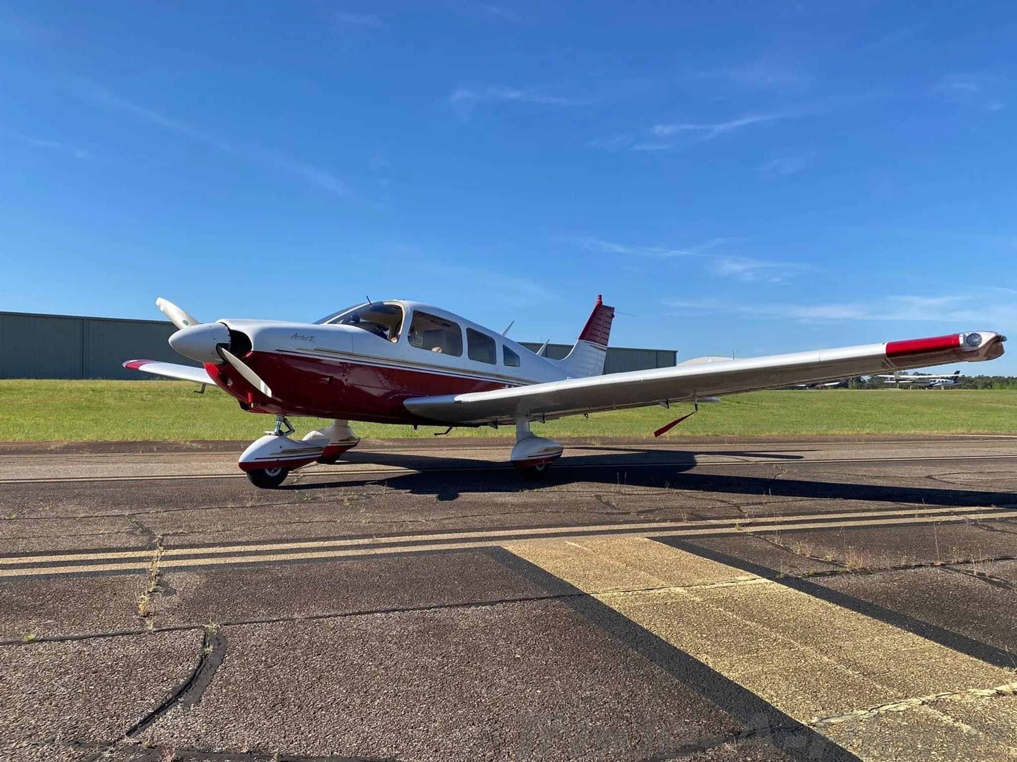 A white and red Piper Arrow II (N926CK) is parked on an asphalt runway with a building in the background.