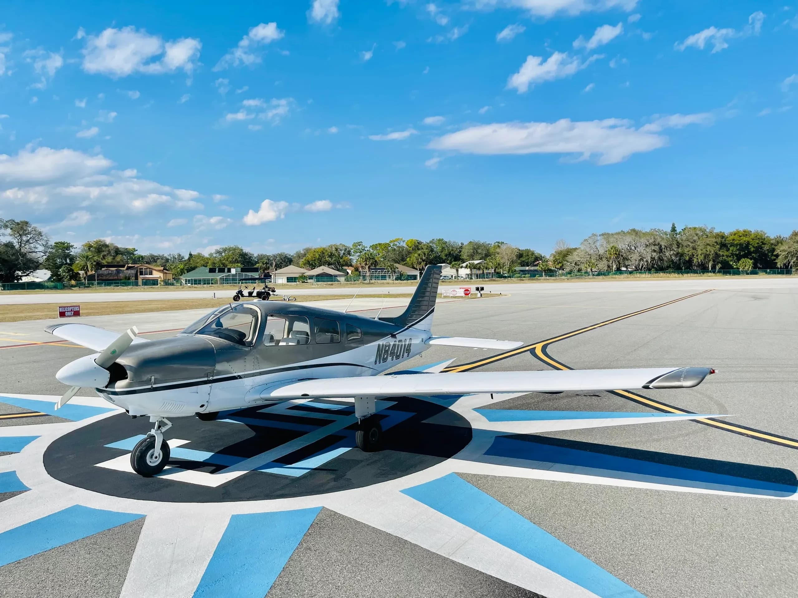 A gray and white single-engine aircraft, registration N84014, parked on a blue and white marked tarmac under a blue sky.