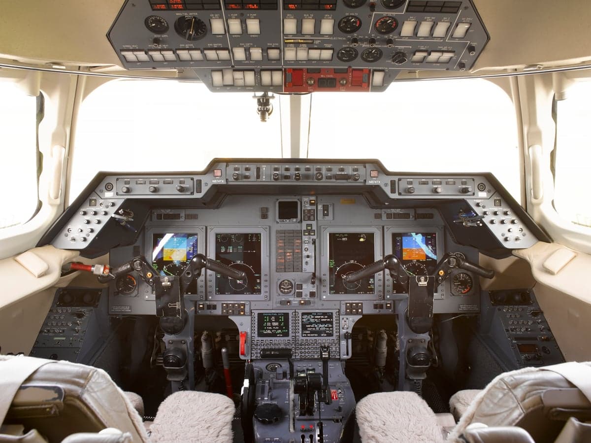 The cockpit of a business jet features multiple digital displays and an overhead panel.