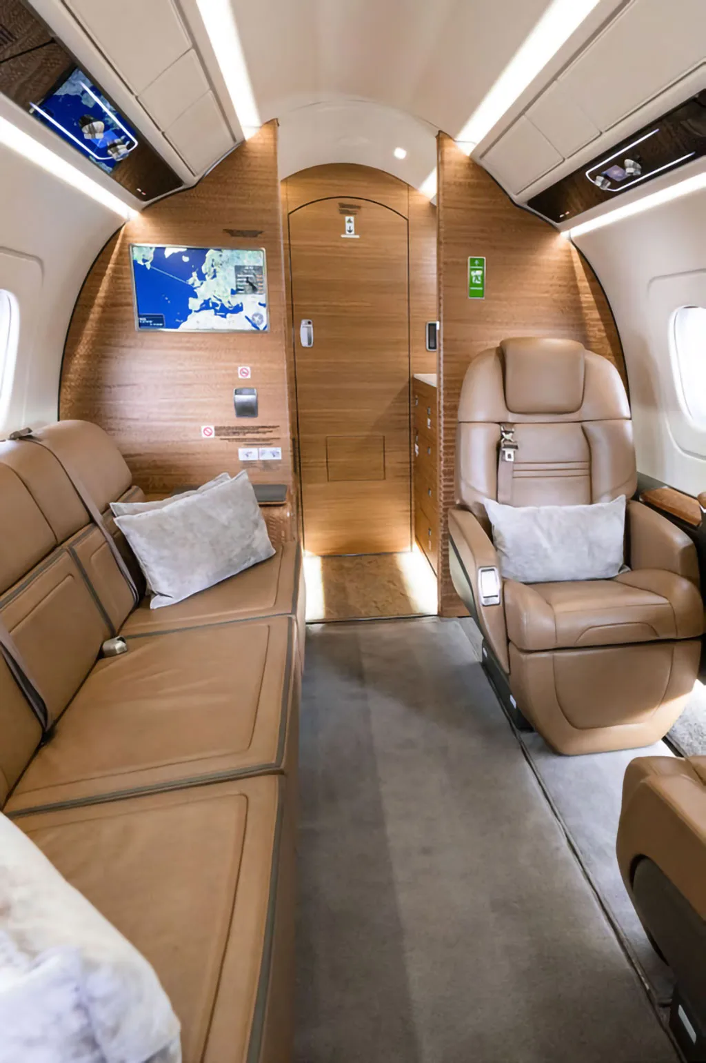 The rear section of a business jet cabin with a tan leather sofa, an individual seat, and a wooden bulkhead.